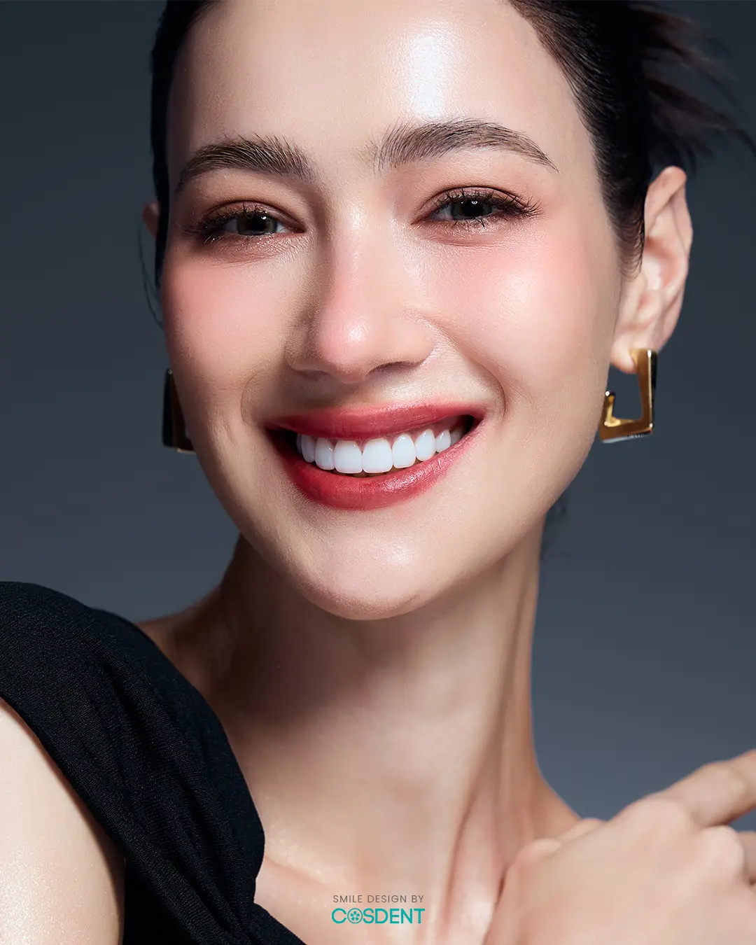 หญิงสาวยิ้มในชุดสีดำและต่างหูสีทอง